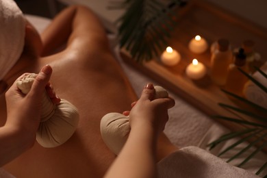 Photo of Woman receiving back massage with herbal bags in spa salon, closeup