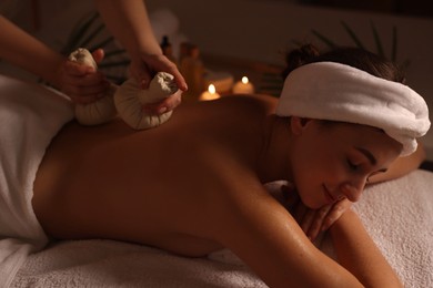 Photo of Young woman receiving back massage with herbal bags in spa salon