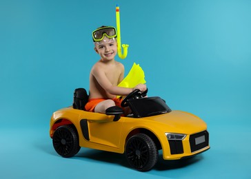 Photo of Cute little boy in beachwear with snorkeling equipment and toy car on light blue background