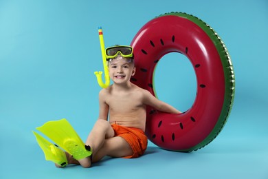 Photo of Cute little boy in beachwear with snorkeling equipment and inflatable ring on light blue background