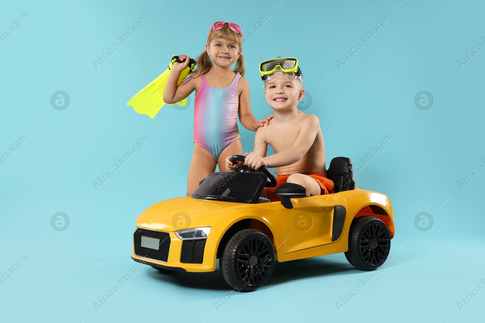 Photo of Cute little kids in beachwear with toy car on light blue background