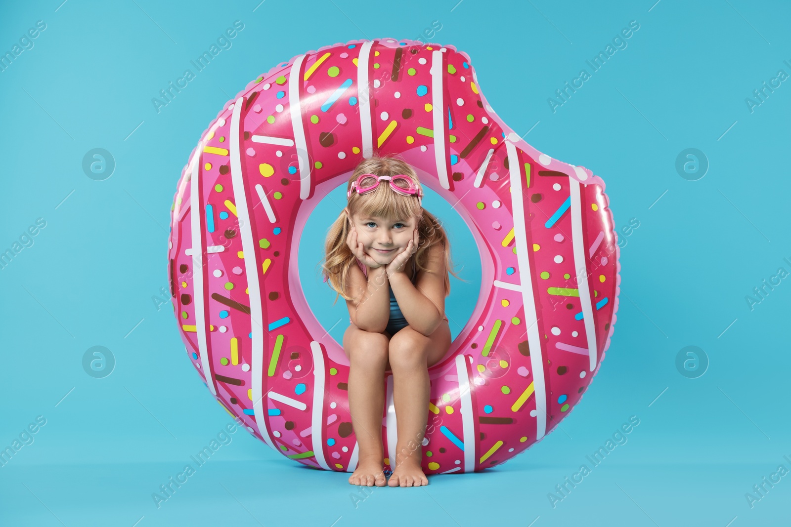 Photo of Cute little girl in beachwear with diving mask and inflatable ring on light blue background