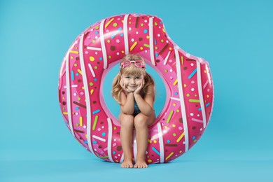 Cute little girl in beachwear with diving mask and inflatable ring on light blue background