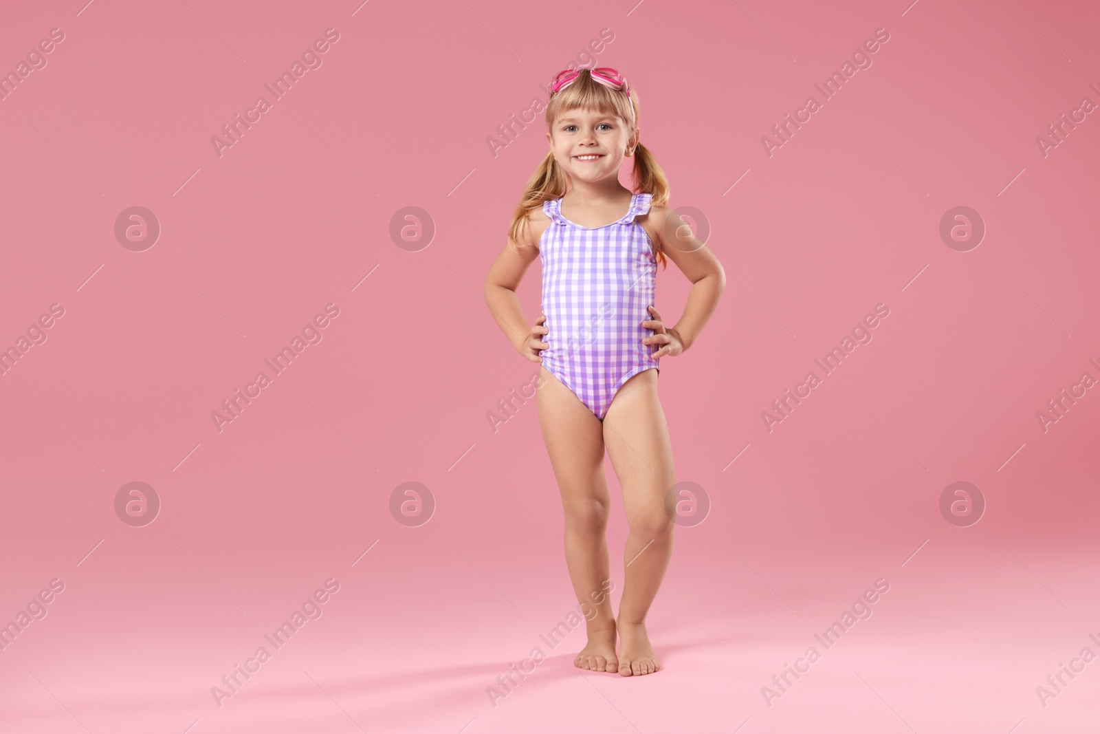 Photo of Cute little girl in beachwear with diving mask on pink background