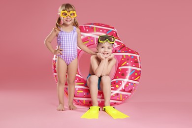 Photo of Cute little kids in beachwear with inflatable ring on pink background