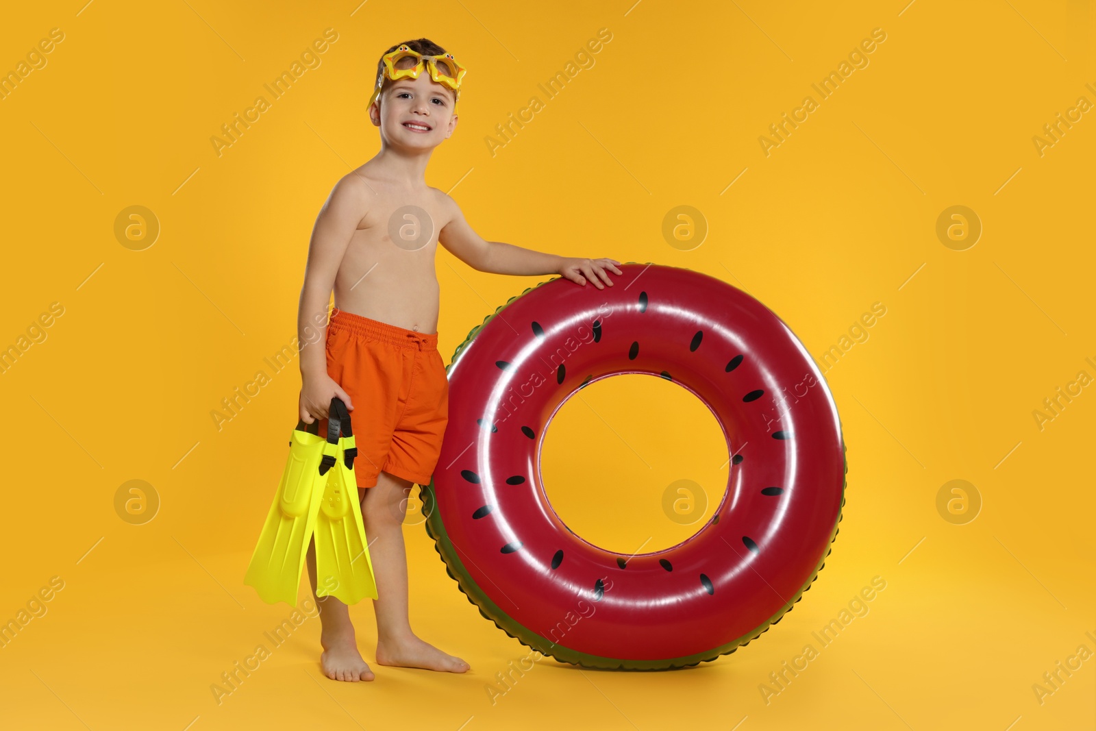 Photo of Cute little boy in beachwear with diving mask, flippers and inflatable ring on orange background