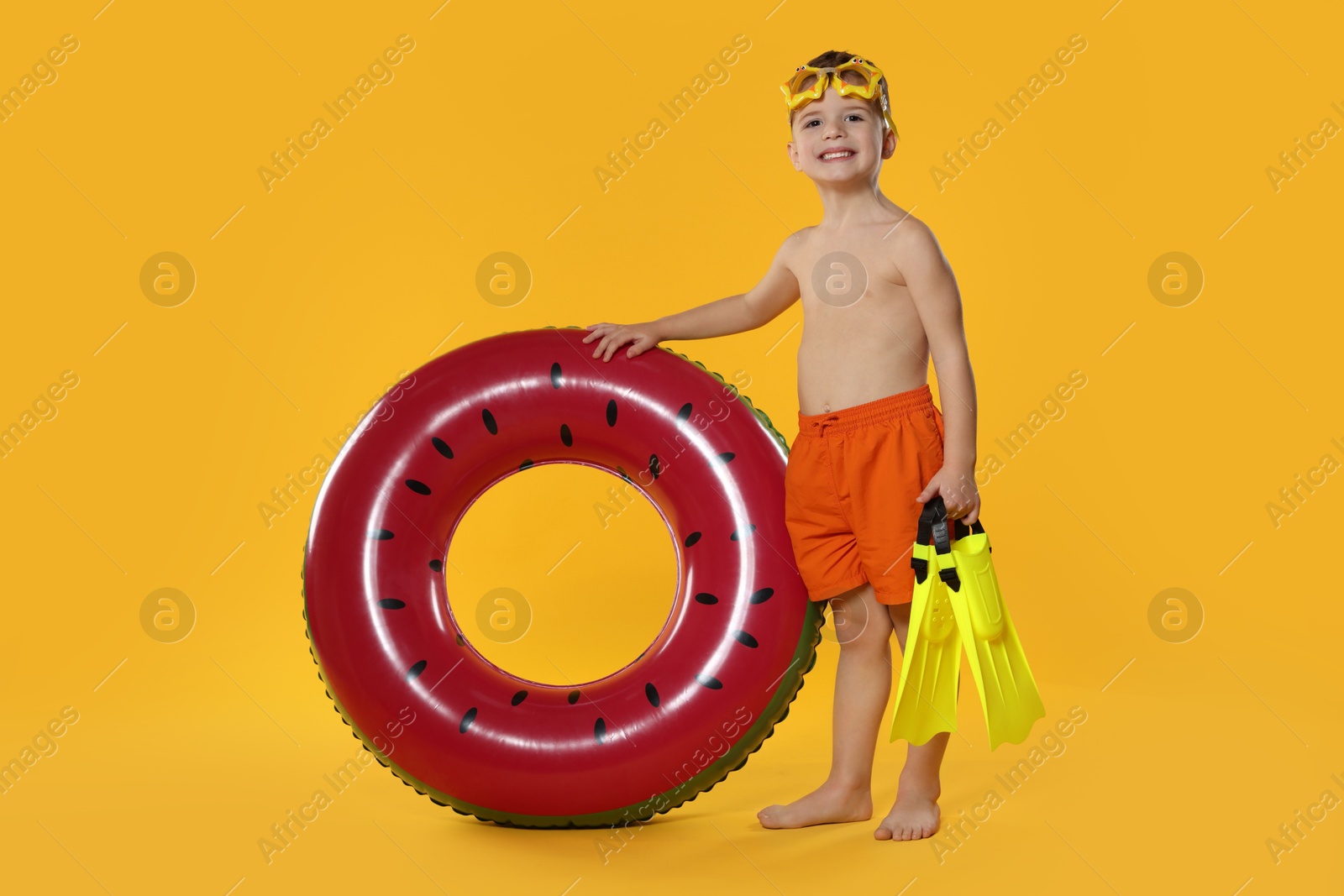 Photo of Cute little boy in beachwear with diving mask, flippers and inflatable ring on orange background