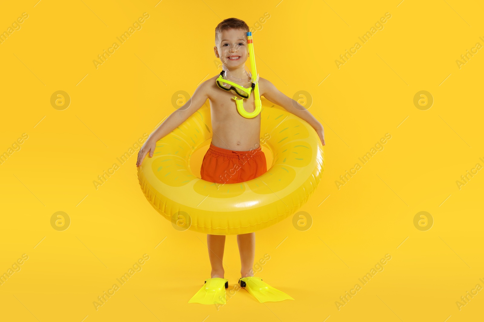 Photo of Cute little boy in beachwear with snorkeling equipment and inflatable ring on orange background