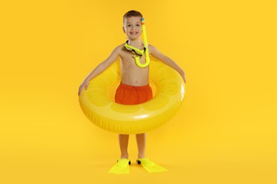 Cute little boy in beachwear with snorkeling equipment and inflatable ring on orange background