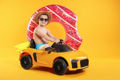 Photo of Cute little boy in beachwear with inflatable ring and toy car on orange background