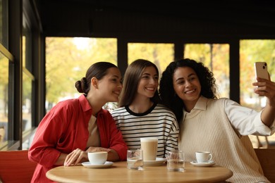 Happy friends taking selfie during coffee meeting in cafe