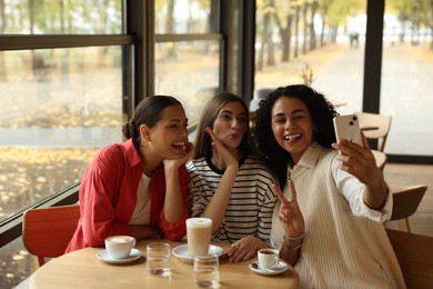 Photo of Happy friends taking selfie during coffee meeting in cafe