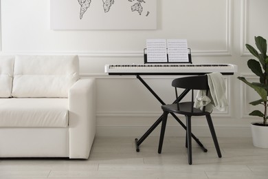 Photo of Synthesizer with music sheets and chair near white wall indoors