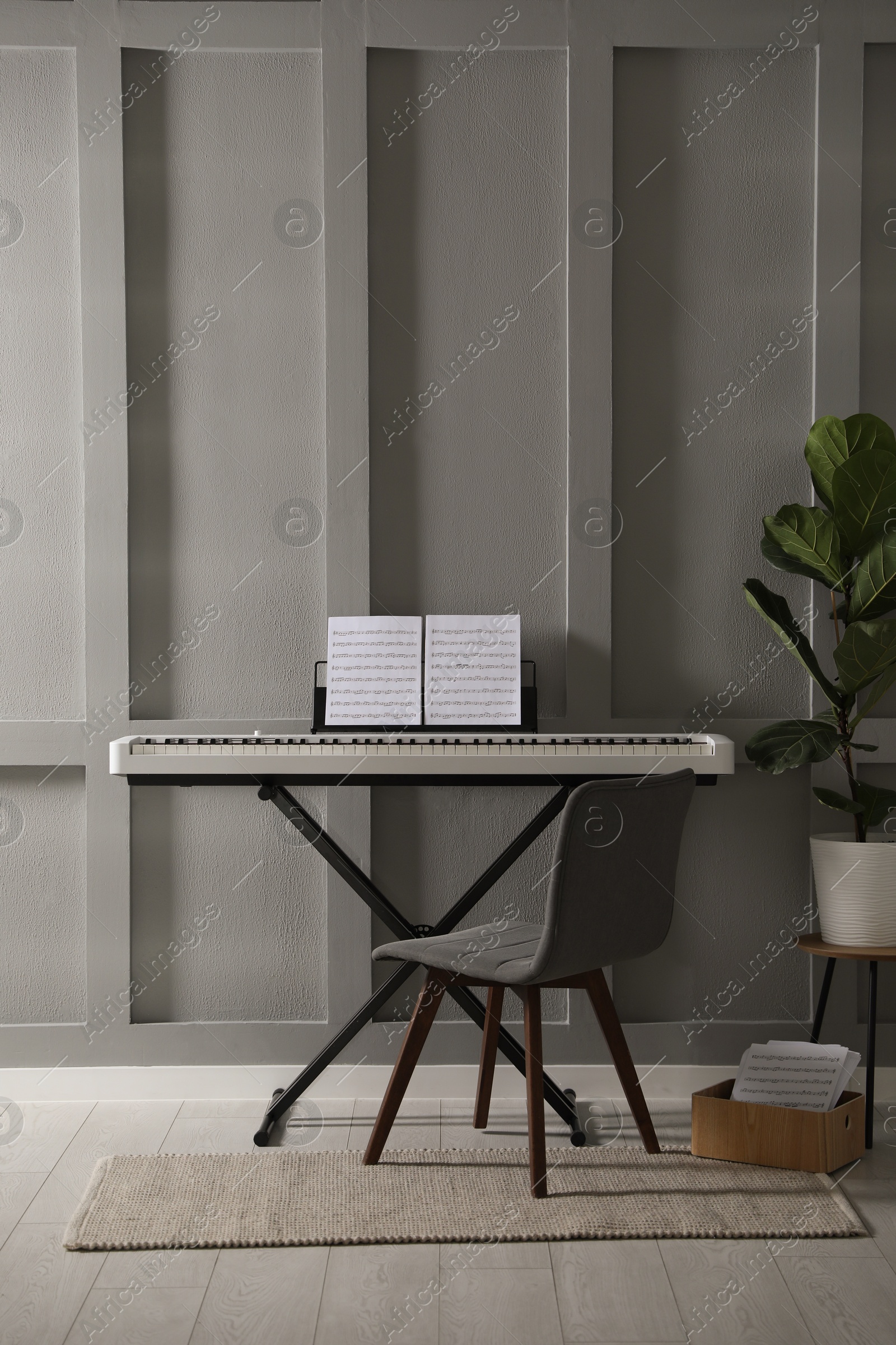 Photo of Synthesizer with music sheets and chair near grey wall indoors