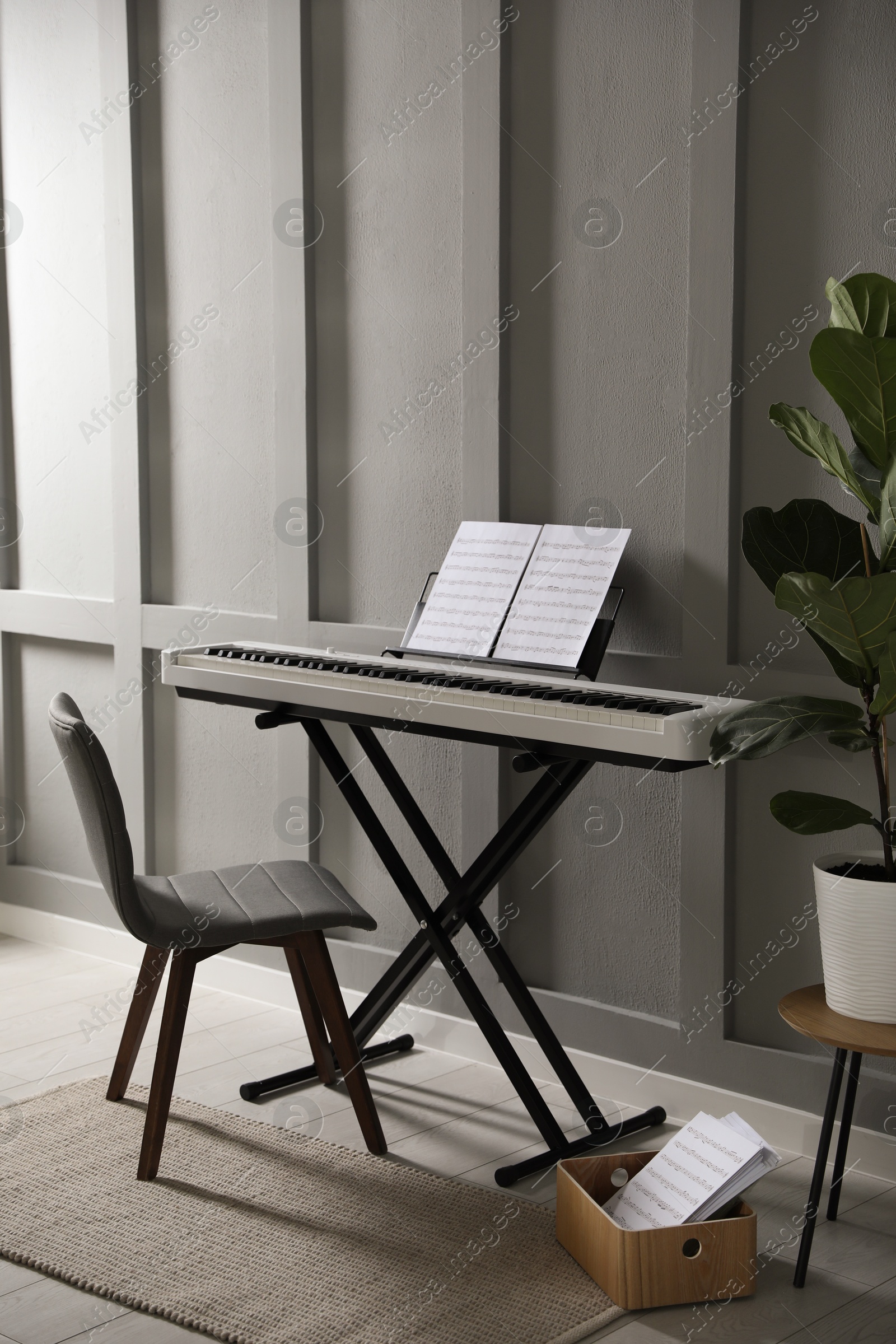 Photo of Synthesizer with music sheets and chair near grey wall indoors