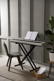 Photo of Synthesizer with music sheets and chair near grey wall indoors