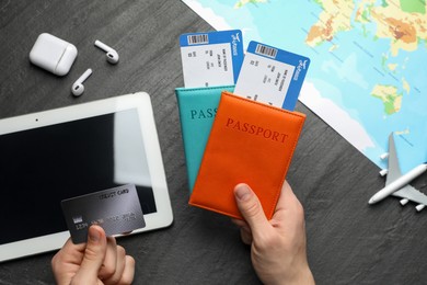 Photo of Travel agency. Man with passports, flight tickets and credit card at dark textured table, top view