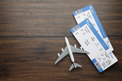 Photo of Travel agency. Flight tickets and plane model on wooden table, flat lay. Space for text