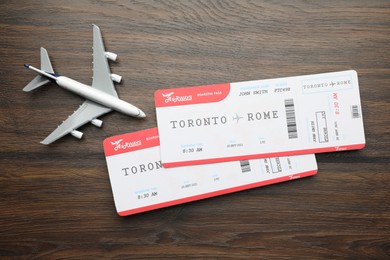 Photo of Travel agency. Flight tickets and plane model on wooden table, flat lay