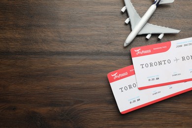 Photo of Travel agency. Flight tickets and plane model on wooden table, flat lay. Space for text