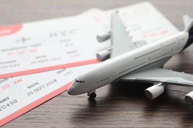 Photo of Travel agency. Flight tickets and plane model on wooden table, closeup