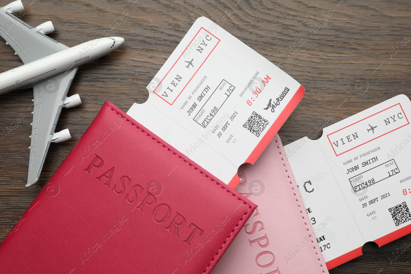 Photo of Travel agency. Flight tickets, passports and plane model on wooden table, flat lay