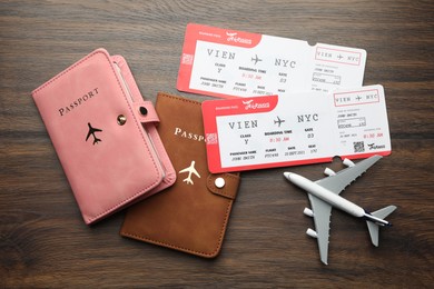 Photo of Travel agency. Flight tickets, passports and plane model on wooden table, flat lay