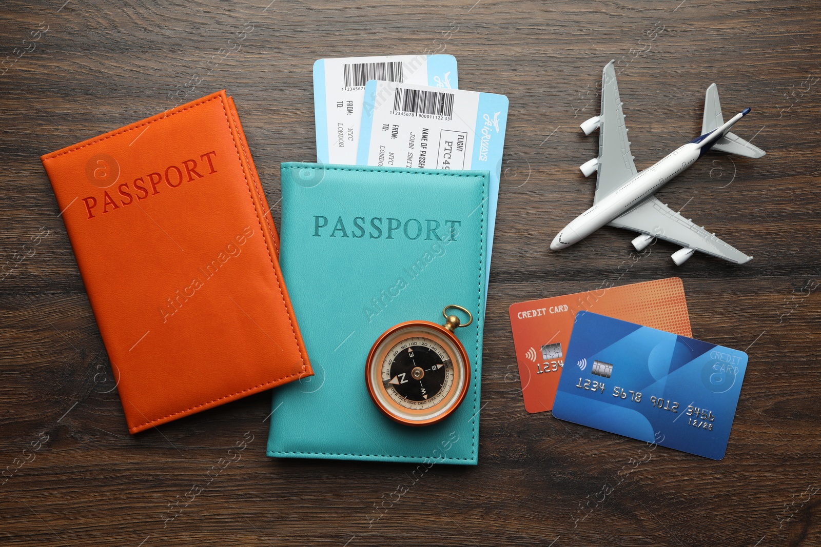 Photo of Travel agency. Flight tickets, passports, compass, credit cards and plane model on wooden table, flat lay