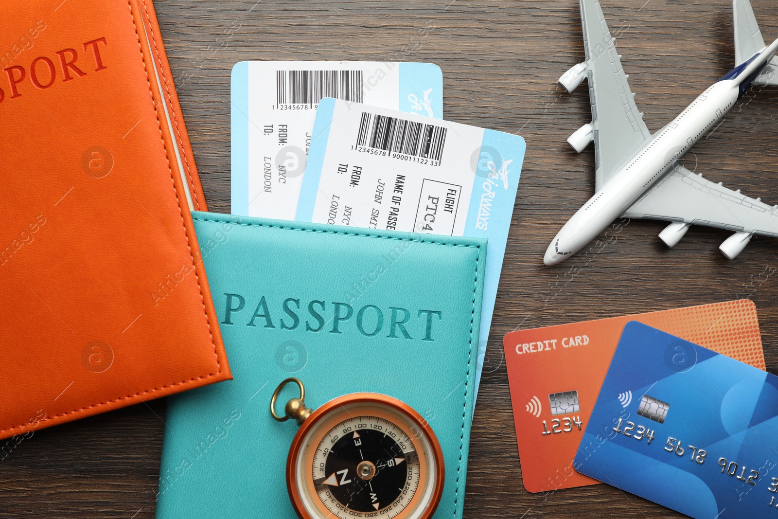 Photo of Travel agency. Flight tickets, passports, compass, credit cards and plane model on wooden table, flat lay