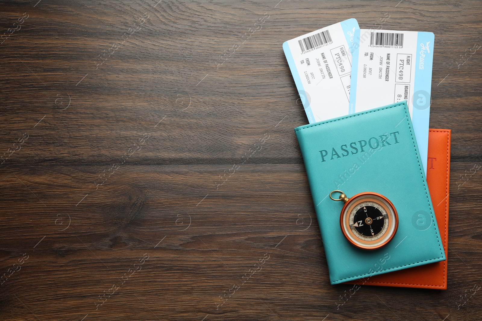 Photo of Travel agency. Flight tickets, passports and compass on wooden table, flat lay. Space for text