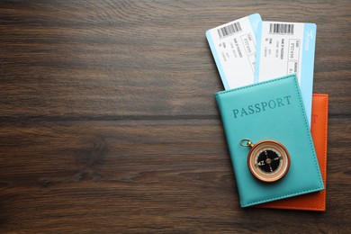 Photo of Travel agency. Flight tickets, passports and compass on wooden table, flat lay. Space for text