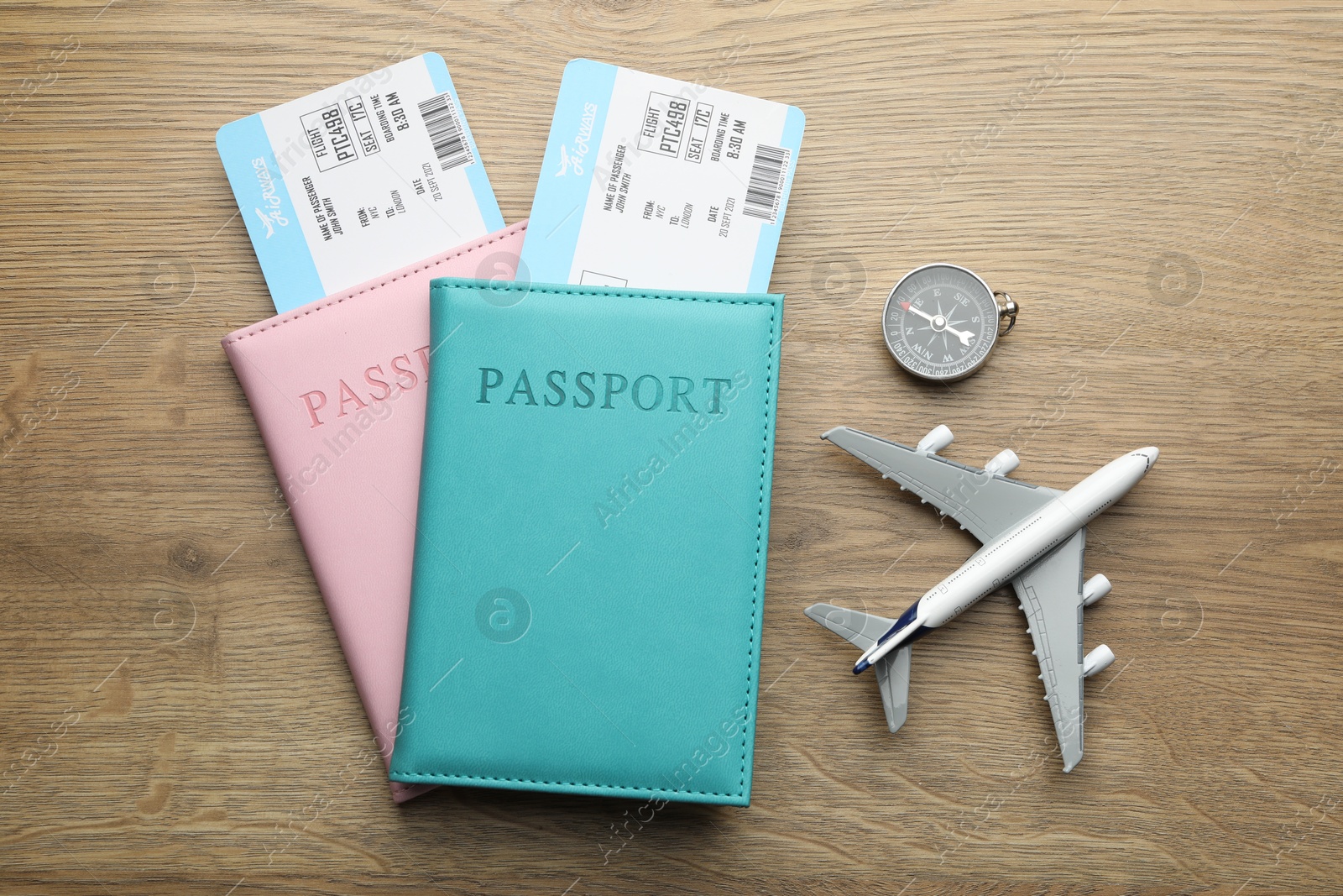 Photo of Travel agency. Flight tickets, passports, compass and plane model on wooden table, flat lay