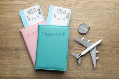 Travel agency. Flight tickets, passports, compass and plane model on wooden table, flat lay