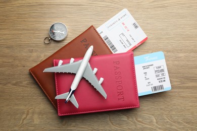 Photo of Travel agency. Flight tickets, passports, compass and plane model on wooden table, flat lay