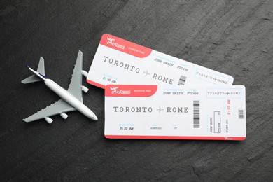 Photo of Travel agency. Flight tickets and plane model on dark textured table, flat lay