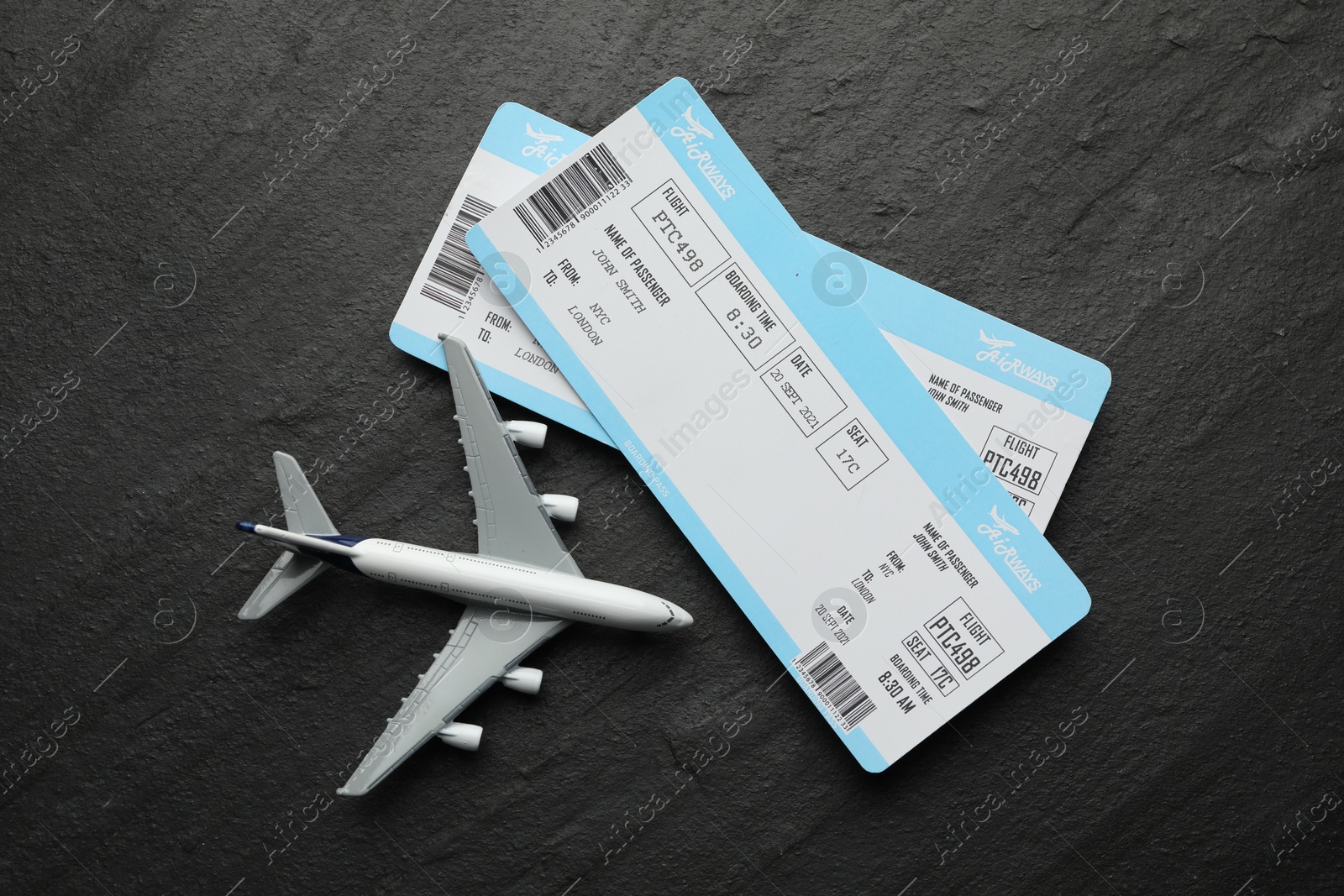 Photo of Travel agency. Flight tickets and plane model on dark textured table, flat lay