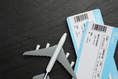 Photo of Travel agency. Flight tickets and plane model on dark textured table, flat lay