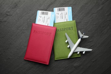 Photo of Travel agency. Flight tickets, passports and plane model on dark textured table, flat lay