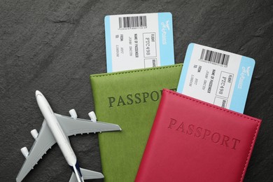 Photo of Travel agency. Flight tickets, passports and plane model on dark textured table, flat lay