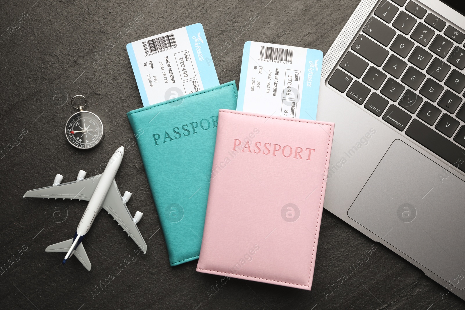 Photo of Travel agency. Flight tickets, passports, plane model, compass and laptop on dark textured table, flat lay