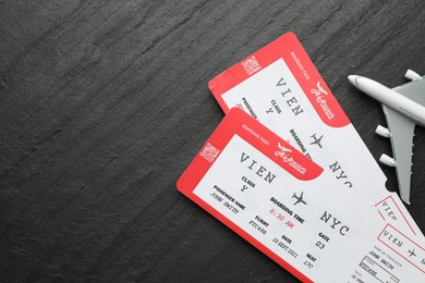 Photo of Travel agency. Flight tickets and plane model on dark textured table, flat lay. Space for text