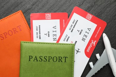 Photo of Travel agency. Flight tickets, passports and plane model on dark textured table, flat lay