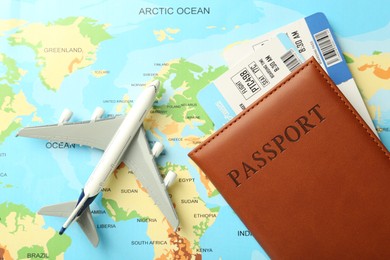 Photo of Passport with tickets and plane model on world map, top view