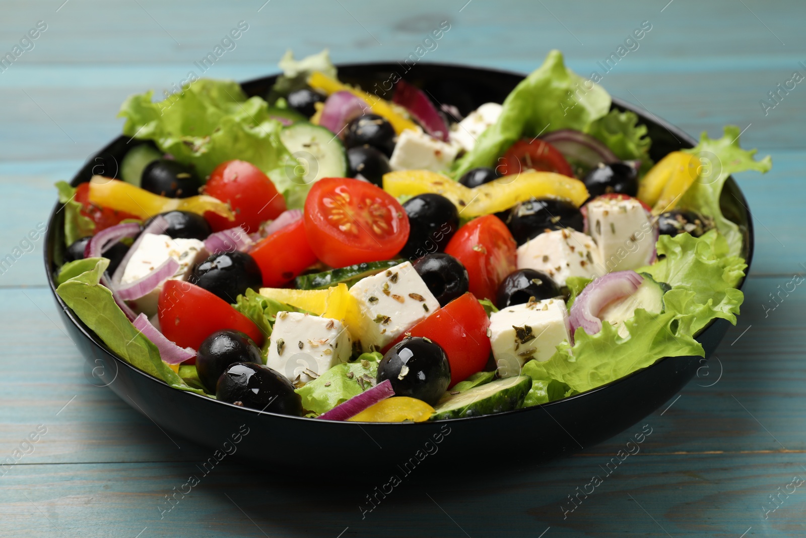 Photo of Delicious fresh Greek salad on light blue wooden table, closeup