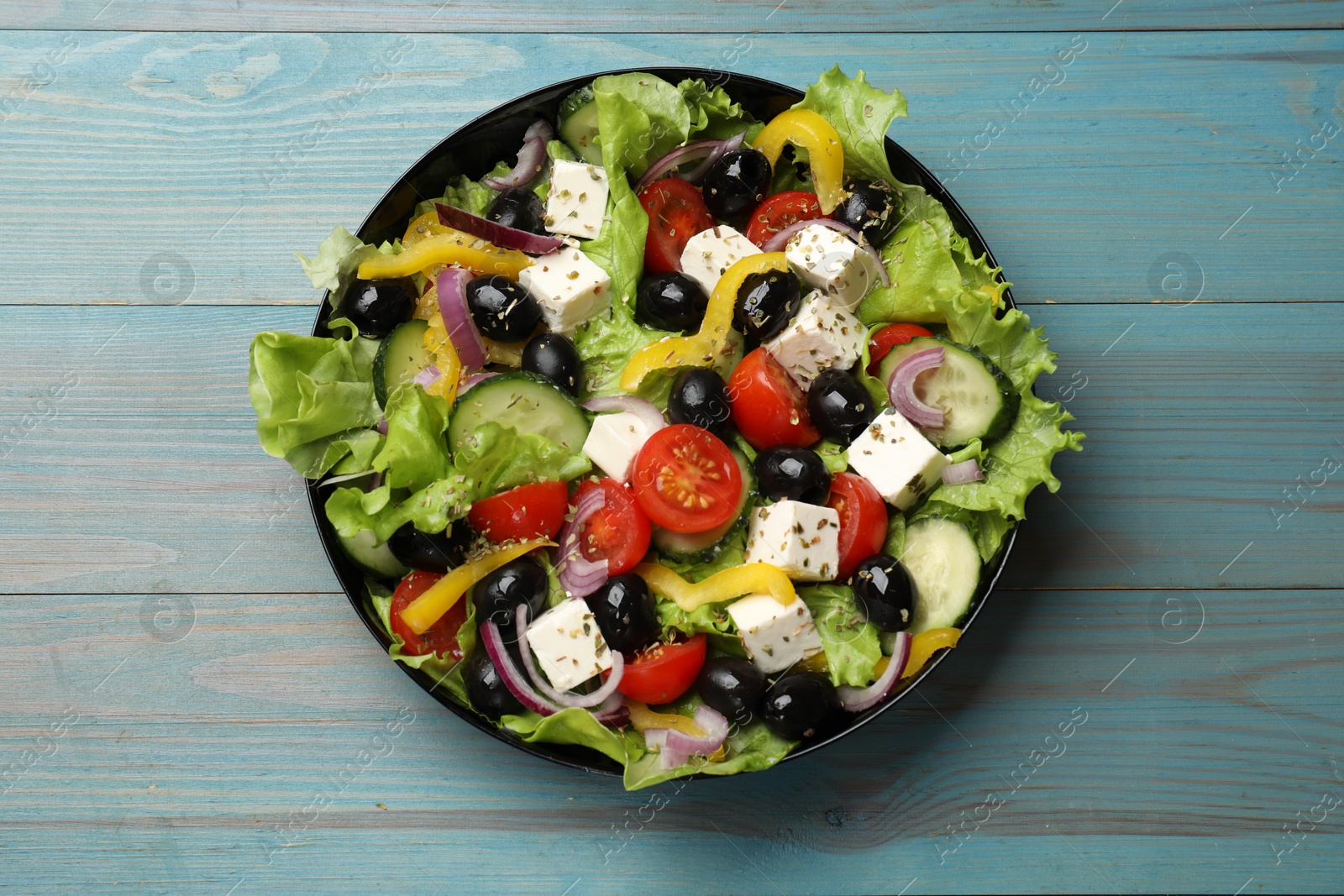 Photo of Delicious fresh Greek salad on light blue wooden table, top view