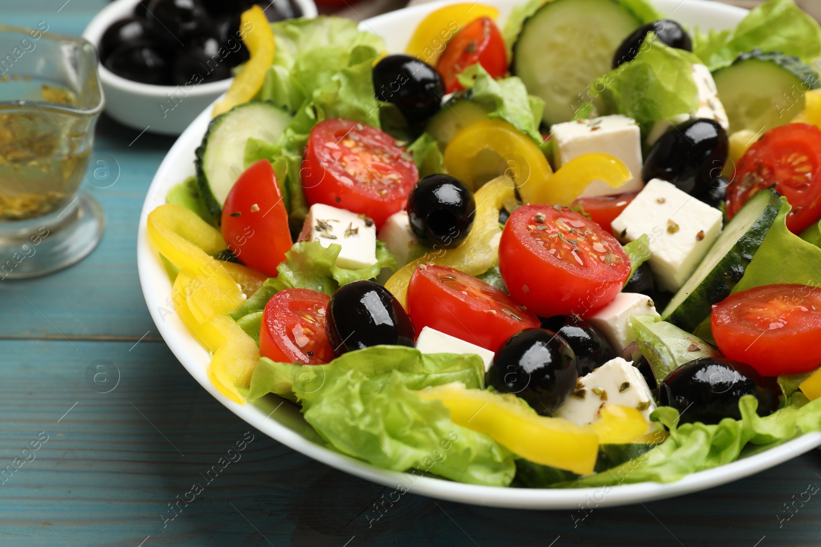 Photo of Delicious fresh Greek salad on light blue wooden table, closeup