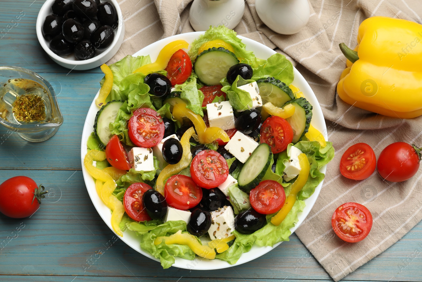 Photo of Delicious fresh Greek salad and ingredients on light blue wooden table, flat lay