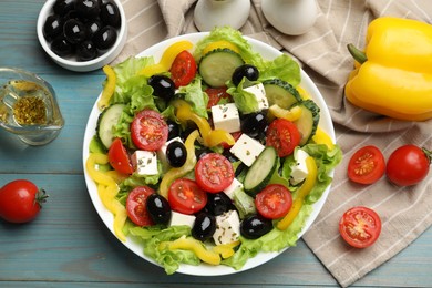 Photo of Delicious fresh Greek salad and ingredients on light blue wooden table, flat lay