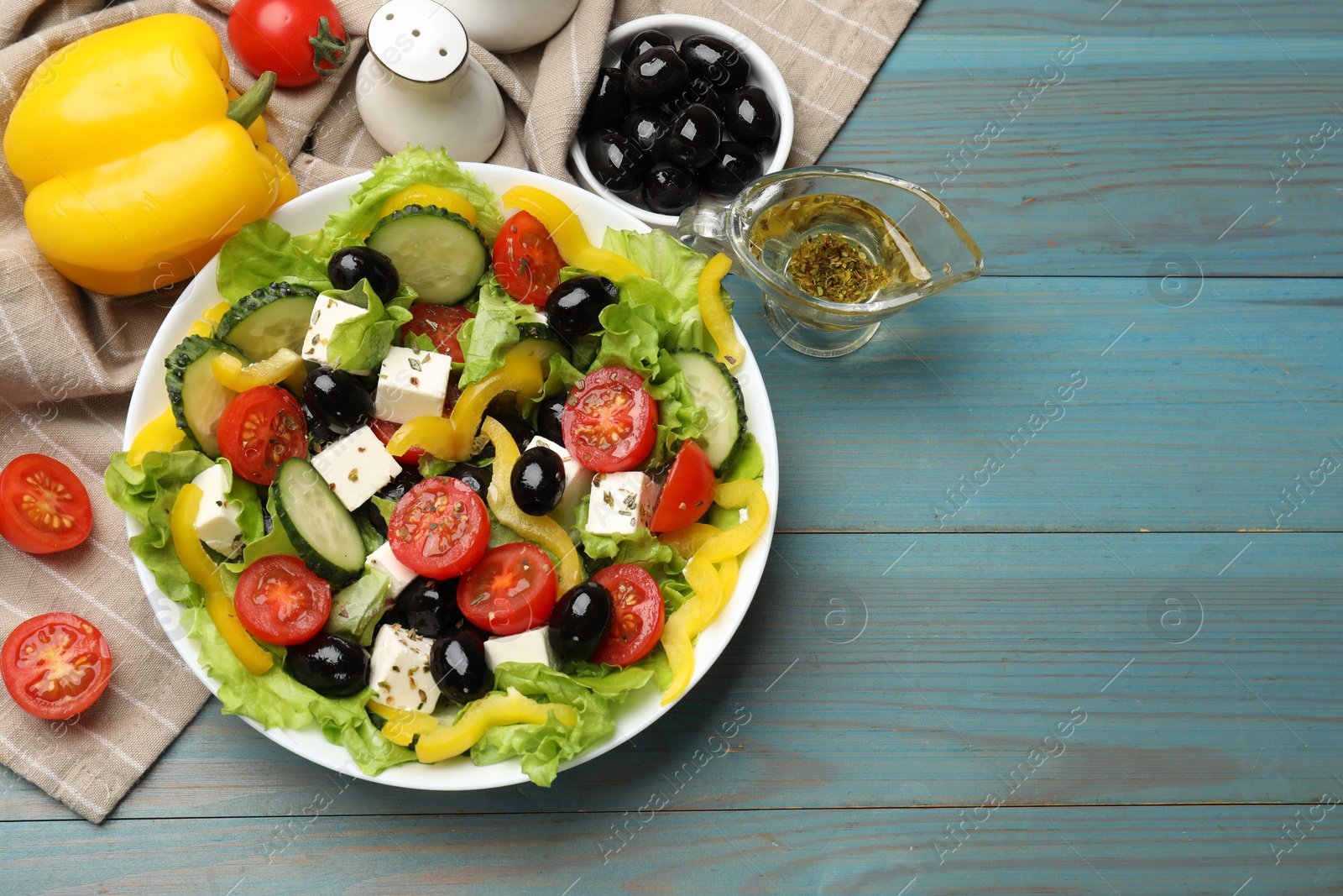 Photo of Delicious fresh Greek salad and ingredients on light blue wooden table, flat lay. Space for text