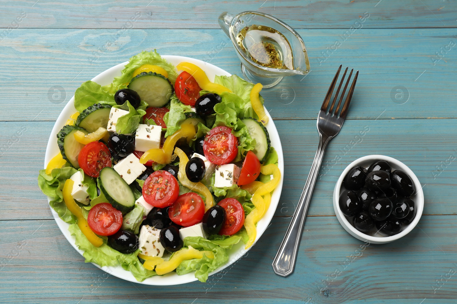 Photo of Delicious fresh Greek salad served on light blue wooden table, flat lay